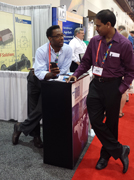 African American man with glasses dressed up at tradeshow conversing with customer at booth.